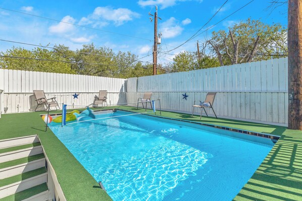 Piscina rectangular con una valla de madera, rodeada de césped y árboles.
