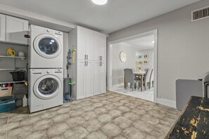 A laundry room with two stacked washing machines, a broom, and cleaning supplies. - Home w/ Outdoor Entertainment Area in San Antonio! (San Antonio)