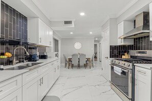 A modern kitchen with white cabinetry, a built-in oven, and a dining area with a table and chairs. - Home w/ Outdoor Entertainment Area in San Antonio! (San Antonio)