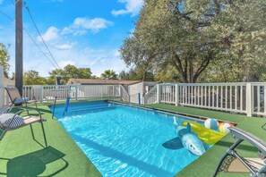 A swimming pool with a shark float, surrounded by a fenced area with a wooden deck and chairs. - Home w/ Outdoor Entertainment Area in San Antonio! (San Antonio)
