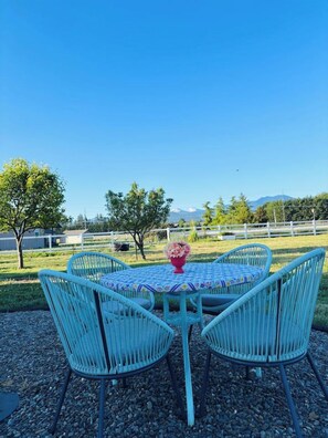 An outdoor seating area with a round table and four chairs, surrounded by a gravel ground. - Redtail Farm Guest House (Sequim)