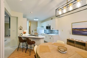 Uma cozinha moderna com armários brancos, uma ilha central e uma área de refeições com mesa redonda e banquetas.