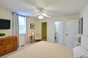 Une chambre à coucher comprenant un lit, une commode, un ventilateur de plafond, une fenêtre avec des stores et une porte.