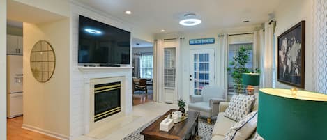 A living room with a fireplace, a television, a sofa, a coffee table, and a door labeled 'BEACH HOUSE'.