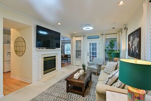 Un salon avec une cheminée, un téléviseur, un canapé, une table basse et une porte sur laquelle est inscrit « MAISON DE PLAGE ».
