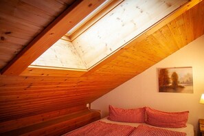 A room with a sloped wooden ceiling, a bed with red checkered bedding, and a painting on the wall. - Thanner Dachmansarde Ambiente (Ofterschwang)