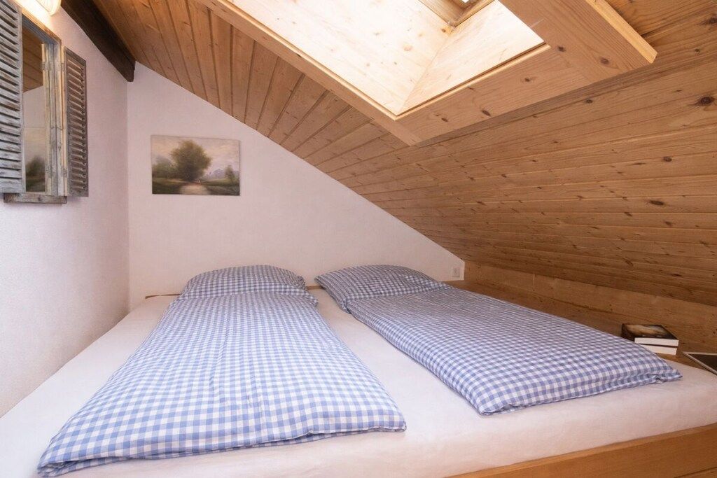 Ein Zimmer mit zwei Einzelbetten, einem Dachfenster, Holzwänden, einem Gemälde und einem kleinen Nachttisch.