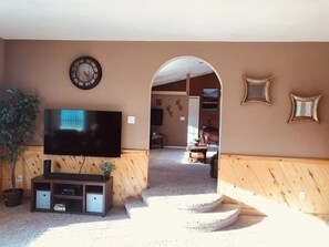 Ein Wohnzimmer mit Flachbildfernseher, Holzvertäfelung, einer Treppe und einer Tür zu einem anderen Raum.
