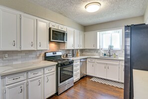 A kitchen with white cabinetry, a stainless steel refrigerator, a microwave, an oven, and a gas stove. - Modern Galveston Retreat Near Beach, Strand & Pier (Galveston)