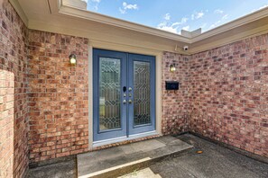A two-door entrance with a brick wall, a small porch, and a security camera. - Modern Galveston Retreat Near Beach, Strand & Pier (Galveston)