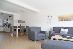A modern living room with a sofa, armchair, and coffee table. There is a dining area with chairs and a table. A lamp and artwork are on the wall. - Terraced house with 2 bedrooms (Sylt Ost\/ Tinnum)