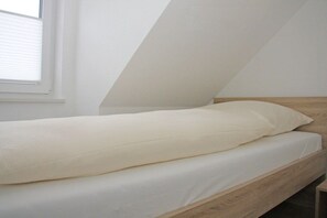 A single bed with a wooden headboard in a room with sloped ceilings. - Terraced house with 2 bedrooms (Sylt Ost\/ Tinnum)