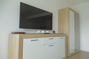 A modern room with a flat-screen TV mounted on a wooden cabinet, a small clock, and a mirror cabinet. - Terraced house with 2 bedrooms (Sylt Ost\/ Tinnum)