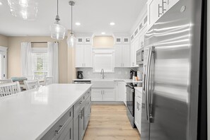 A modern kitchen with white cabinetry, a stainless steel refrigerator, and pendant lighting. - Brand New Retreat Private Pool & Golf Simulator (Hilton Head)