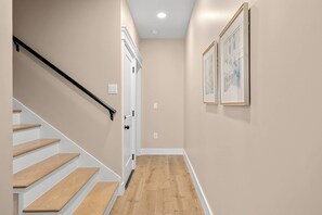 A hallway with a wooden staircase, a white door, and two framed pictures on the wall. - Brand New Retreat Private Pool & Golf Simulator (Hilton Head)