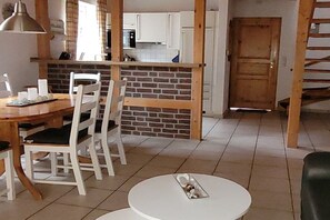 Ein Essbereich mit einem runden Tisch und Stühlen, eine Küche im Hintergrund und eine Holztür.