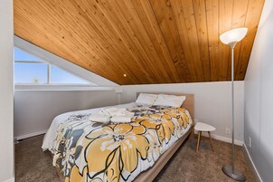 Un dormitorio con techo inclinado, una cama con colcha estampada, una mesita de noche y una lámpara de pie.