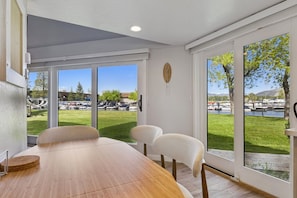 A dining area with a wooden table and chairs, large windows with a view of a park and boats. - 489 Tahoe Keys Blvd, Unit 69 1 Bedroom Condo (South Lake Tahoe)