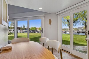 Un comedor con mesa y sillas de madera, ventanas amplias con vista a un parque y barcos.