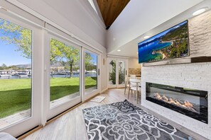 A modern living room with large windows, a fireplace, and a television. - 489 Tahoe Keys Blvd, Unit 69 1 Bedroom Condo (South Lake Tahoe)