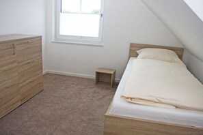 A bedroom with a bed, a dresser, a window, and a small bedside table. - Terraced house with 2 bedrooms (Sylt Ost\/ Tinnum)