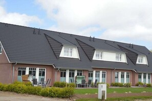 A two-story building with a sloped roof, multiple windows, and a small outdoor seating area with chairs and a table. - Terraced house with 2 bedrooms (Sylt Ost\/ Tinnum)