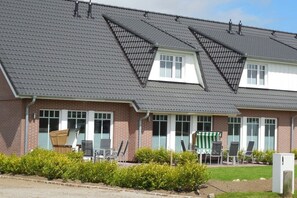 A two-story building with a sloped roof, multiple windows, and a small outdoor seating area with chairs and a table. - Terraced house with 2 bedrooms (Sylt Ost\/ Tinnum)