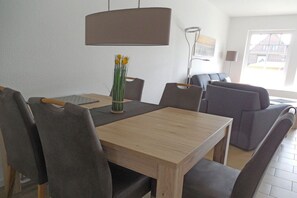 A dining area with a wooden table, grey upholstered chairs, and a vase with yellow flowers. - Terraced house with 2 bedrooms (Sylt Ost\/ Tinnum)