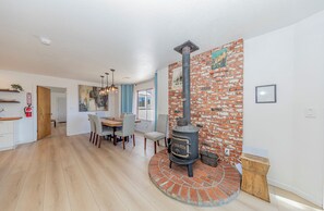 A modern kitchen with a central island, a dining area with a wooden table and chairs, and a brick wall with a poster. - Oak-Studded Mountain Escape with Hot Tub & Game Room (Mariposa)