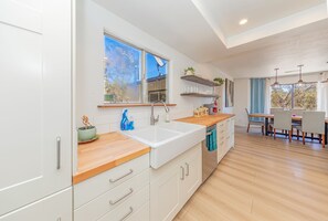 A modern kitchen with white cabinetry, a double sink, and wooden countertops. There are shelves above the sink with dishes and a potted plant. - Oak-Studded Mountain Escape with Hot Tub & Game Room (Mariposa)