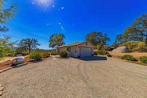 Einbungalow mit Garage, umgeben von Kiesweg, Bäumen und einem großen Felsen.