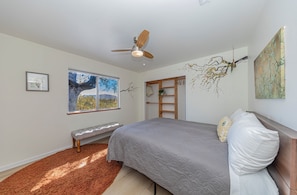 Ein Schlafzimmer mit Bett, einer Bank, einem Deckenventilator, einem Fenster mit Ausblick und Kunstwerken an den Wänden.