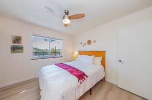 Un dormitorio con cama, ventilador de techo, ventana con vistas y una puerta.