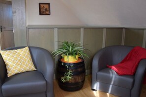 A room with two leather armchairs, one with a yellow patterned pillow and the other with a red throw. A wooden barrel with a plant is placed between them. - Holiday apartment in Epfig with swimming pool (Epfig)