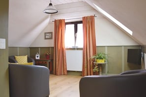 A cozy attic room with a sloped ceiling, a window with curtains, a radiator, a small table with a plant, and a sofa with cushions. - Holiday apartment in Epfig with swimming pool (Epfig)