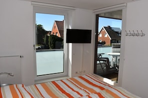 Een kamer met een bed, een aan de muur bevestigde televisie en een schuifdeur die leidt naar een buitenruimte met een tafel en stoelen.