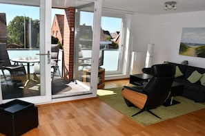 Un salon moderne avec une porte vitrée donnant sur un balcon, un canapé en cuir noir et une petite table avec des tasses.