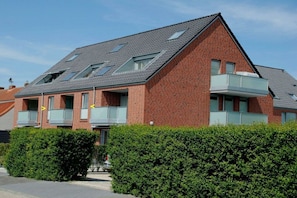 En modern bostadsbyggnad med ett sluttande tak, flera balkonger och en fasad av tegel.
