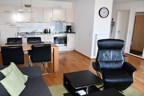 A modern living room with a sofa, a dining table, and a black leather chair. - Holiday apartment with 1 bedroom (Norderney)