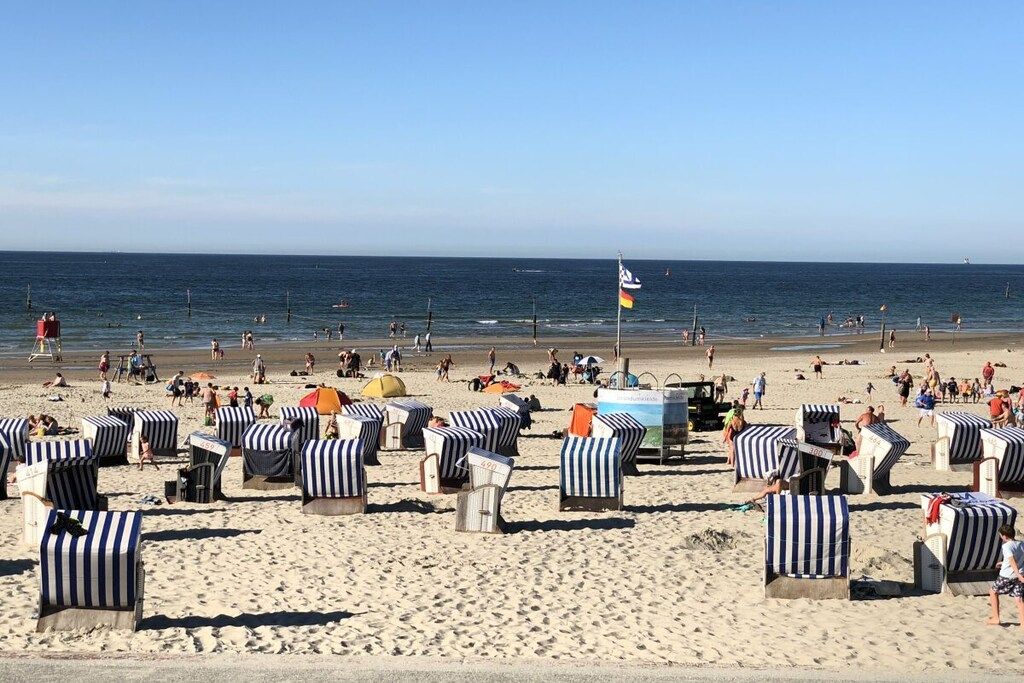 Een strand met gestreepte ligbedden en parasols, een vlag, en mensen in de verte.