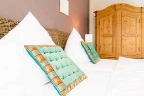 A bed with white pillows and a teal accent pillow, a bedside lamp, and a wooden wardrobe in a room with a woven headboard. - Holiday apartment *blanco* Willingen (Willingen)