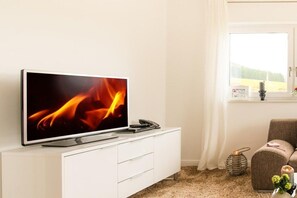 A flat-screen TV on a white cabinet, a wicker basket with candles, and a brown chair. - Holiday apartment *blanco* Willingen (Willingen)