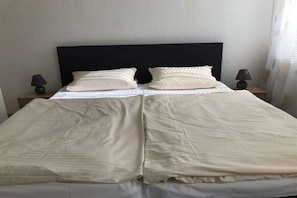 Ein Bett mit schwarzem Kopfteil, zwei Nachttischlampen und einer schlichten Bettdecke.