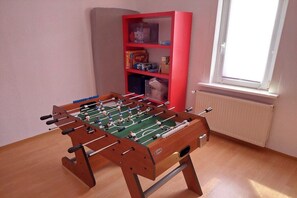 A room with a foosball table, a red bookshelf, and a window with blinds. - Holiday apartment with 2 bedrooms (Bad Tabarz)