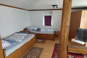 A room with two wooden beds, a window with a purple curtain, a wooden wardrobe, and a chair with a grey blanket. - Holiday apartment with 2 bedrooms (Bad Tabarz)
