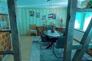 A dining area with a round table, chairs, a vase with flowers, and a window with blinds. - Holiday apartment with 2 bedrooms (Bad Tabarz)