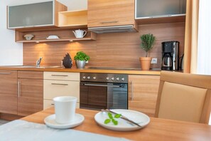 Une cuisine moderne avec des meubles en bois, un four encastré, une machine à café et une table à manger avec une tasse et une assiette.