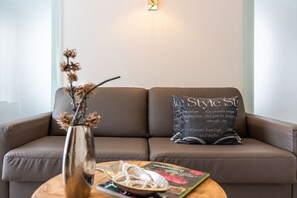 Un canapé en cuir marron avec un coussin orné de motifs textuels, un vase contenant des fleurs séchées et un livre posé sur une table ronde en bois.
