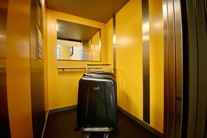 En smal hall med en svart resväska i mitten, en spegel på väggen och en dörr på höger sida.