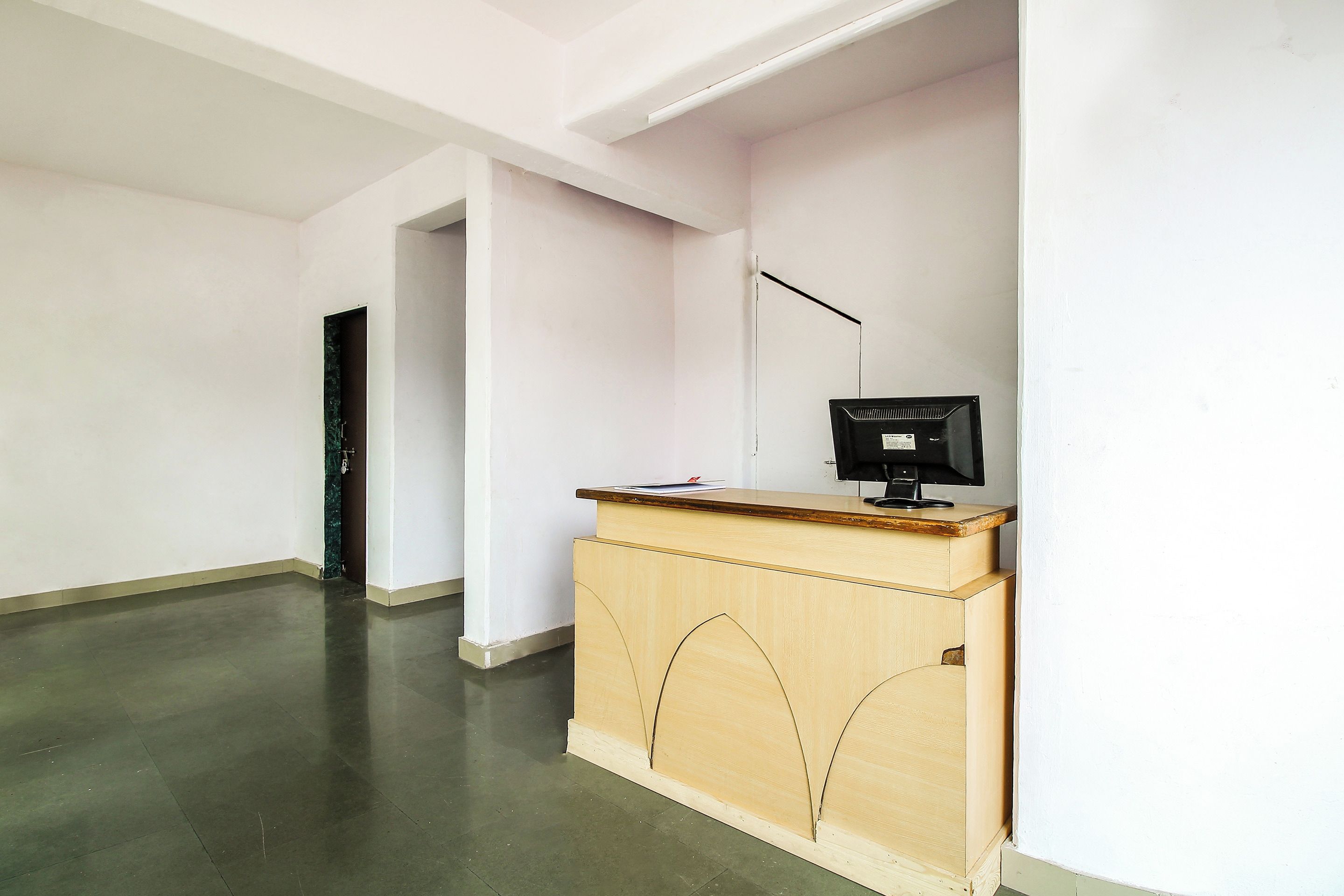 A room with a wooden desk, a computer, and a door leading to another room.